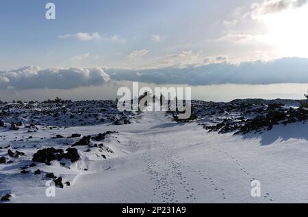 Tierpfade auf malerischen Pfaden, die Vulkanfelsen überqueren, schneebedeckt im Ätna-Nationalpark, Sizilien, Italien Stockfoto