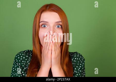 Junge, rothaarige Frau mit grünem Hintergrund schockiert überrascht Stockfoto
