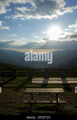 Picknicktisch mit Blick auf das Jerte-Tal bei Sonnenuntergang im Winter, vertikal mit Sonne zwischen den Wolken Stockfoto