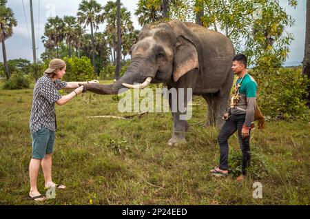 Ein kambodschanischer Mahout, geschmückt mit buddhistischen Amuletten, um Gefahren abzuwehren, steht neben seinem Elefanten auf Buschland in Phumi Khna, Siem Reap Province, Cambo Stockfoto