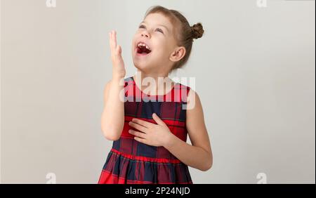 Lachend und bewundernswert mit einem Kind mit offenem Mund, das mit erhobener Hand aufblickte, einem weißen Mädchen von 6 7 Jahren im roten Karomuster Stockfoto