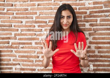 Junge Teenagerin, die über einer Ziegelmauer steht und Hände wegbewegt. Sie zeigt Weigerung und Verleugnung mit Angst und ekelhaftem Gesichtsausdruck. Halt und Forbi Stockfoto
