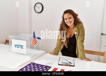 Junge, wunderschöne hispanische Frau, Wahlpräsidentin, die selbstbewusst am Wahlkollegium lächelt Stockfoto