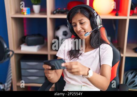 Junge, wunderschöne hispanische Frau, die auf der Straße Videospiele mit dem Smartphone spielt Stockfoto
