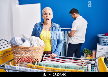 Hispanische Mutter und Sohn hängen Kleidung an der Wäscheleine erschrocken und erstaunt mit offenem Mund für Überraschung, Unglauben Gesicht Stockfoto