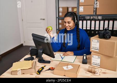 Junge hispanische Frau E-Commerce Call Center Agent mit Videoanruf halten Apfel im Büro Stockfoto
