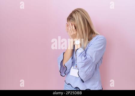 Junge weiße Geschäftsfrau, die beim Weinen einen einen ausweis mit traurigem Gesichtsausdruck trägt, der das Gesicht mit Händen verdeckt. Depressionskonzept. Stockfoto