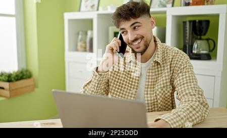 Junger arabischer Mann, der zu Hause mit einem Laptop über ein Smartphone spricht Stockfoto