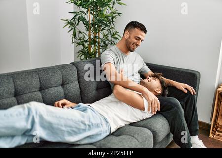 Zwei hispanische Männer, die zu Hause lächeln und selbstbewusst auf dem Sofa sitzen Stockfoto