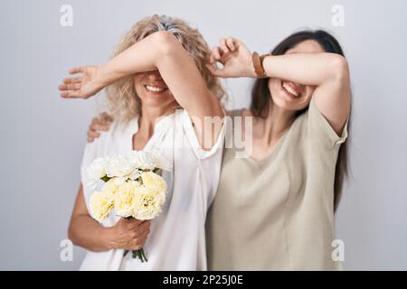 Mutter und Tochter halten einen Strauß weißer Blumen, lächelnd und fröhlich, während sie gucken, mit Händen, die Gesicht zeigen. Überrascht und verlassen Stockfoto