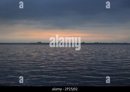 Bewölkter Sonnenuntergang mit Schiffen vor Anker in Manila Bay, Philippinen Stockfoto