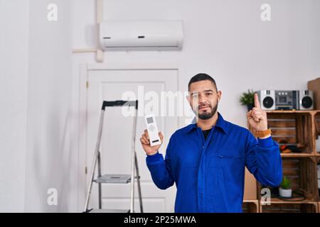 Ein hispanischer Techniker, der mit Klimaanlage arbeitet, war überrascht von einer Idee oder einer Frage, die mit dem Finger auf ein glückliches Gesicht zeigt, Nummer eins Stockfoto