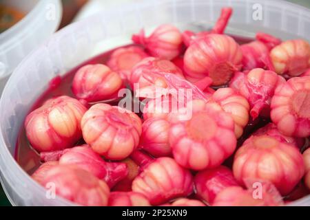 Knoblauch gebeizt in Rot Rote Beete juce an einem Lebensmittelmarkt. Stapel der ganzen Knoblauch Köpfe gesalzen in einem Eimer zum Verkauf Stockfoto