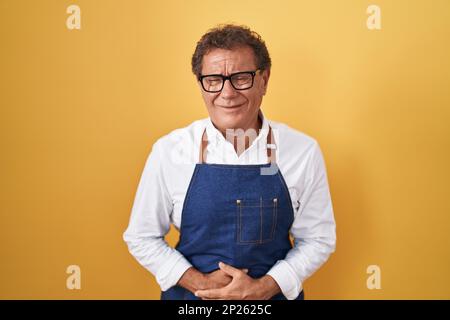 hispanischer Mann mittleren Alters, der eine professionelle Kochschürze mit der Hand auf dem Bauch trägt, weil Verdauungsstörungen, schmerzhafte Krankheit, sich unwohl fühlt. Ache-Konzept. Stockfoto