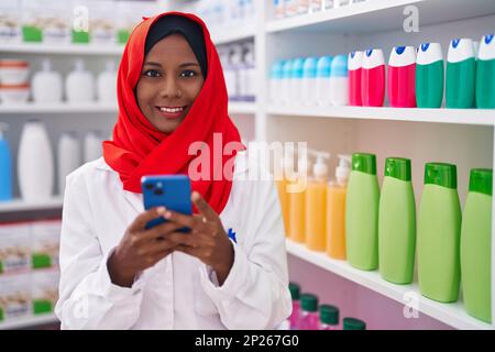 Junge, schöne Apothekerin mit Smartphone, die in der Apotheke arbeitet Stockfoto