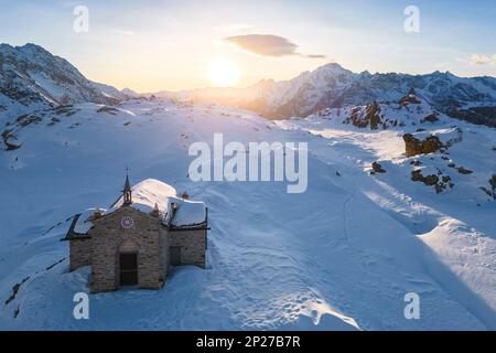 Sonnenuntergang am Alpe Prabello mit Santuario Madonna della Pace im Winter. Lanzada, Valmalenco, Valtellina, Sondrio District, Lombardei, Italien, Europa. Stockfoto