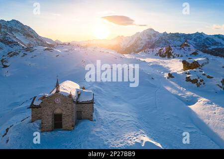 Sonnenuntergang am Alpe Prabello mit Santuario Madonna della Pace im Winter. Lanzada, Valmalenco, Valtellina, Sondrio District, Lombardei, Italien, Europa. Stockfoto