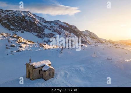 Sonnenuntergang am Alpe Prabello mit Santuario Madonna della Pace im Winter. Lanzada, Valmalenco, Valtellina, Sondrio District, Lombardei, Italien, Europa. Stockfoto