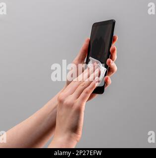 Die Hände wischen das Display des Mobiltelefons mit einem feuchten antibakteriellen Wischtuch ab. Stockfoto