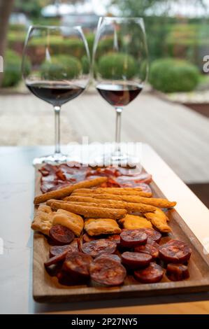 Holzteller mit spanischen Tapas, Choriso-Wurst, Lomo iberico en Brotstangen, serviert mit einem Glas Rotwein, aus nächster Nähe Stockfoto