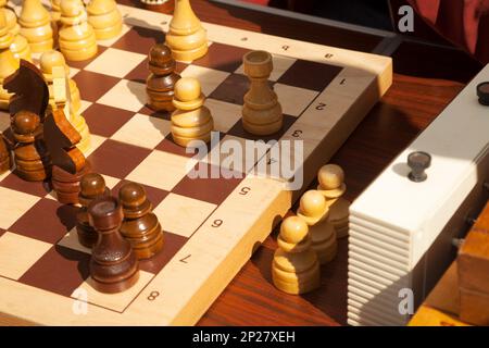 Holz- Schachfiguren auf einem Schachbrett neben einer Uhr während eines Spiels. Strategisches Brettspiel Prozess Stockfoto