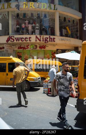 Ramallah, Ramallah und al-Bireh Governorate, Palästina, 8. Juli 2022: Arab Men Walking in Front of a Mall that read 'Bridal' and 'Sweet Night' in a busy Stockfoto