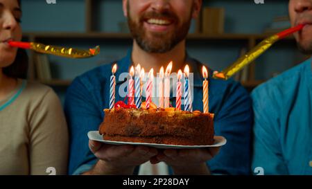 Gekürzte Aussicht Weißer Erwachsener mit glücklichem Bart Mann feiern Geburtstag zu Hause verschiedene afrikanische weiße Freunde gratulieren dem Mann mit festlichem Kuchen Stockfoto