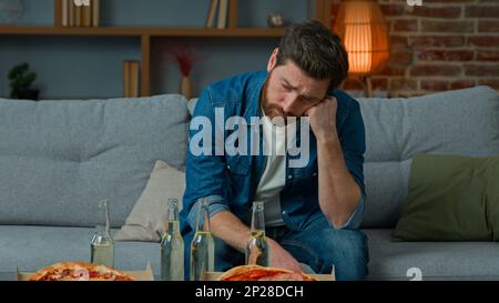 Weißer, erwachsener, alleinstehender Mann, der allein auf der Party sitzt, keine Gäste, einsamer Geburtstag. Trauriger unglücklicher bärtiger Mann in Verzweiflung Krise mittleren Alters Blick auf den Tisch Stockfoto