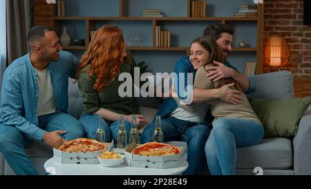 Allein weißer Mann sitzt zu Hause und wartet auf Gäste, multirassische, ethnische, interrassistische Freunde, Überraschungsbesprechungen, sitzen auf der Couch, feiern zusammen Stockfoto
