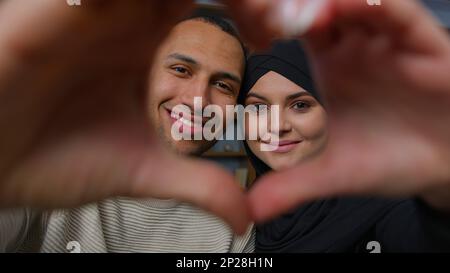 Frisch verheiratete, ethnisch gemischte Ehepaare, afroamerikanischer Mann, mit geliebter arabischer Frau, die durch den Herzrahmen in die Kamera schaut, vereint Ehemann Ehefrau Stockfoto