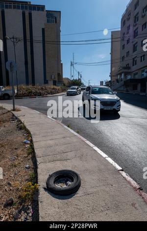 Ramallah, Ramallah und al-Bireh Governorate, Palästina, 20. Juli 2022: Autos auf den Straßen vor einem Reifen voller Müll auf einem Bürgersteig Stockfoto