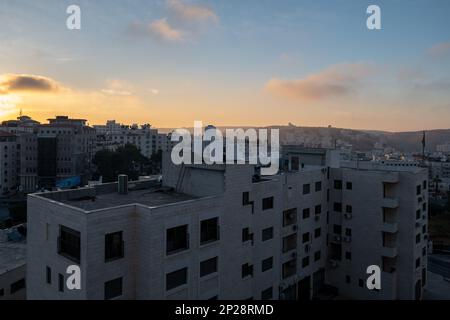 Ramallah, Ramallah und al-Bireh Governorate, Palästina, 13. Juli 2022: Dunkles Stadtbild von Ramallah bei Sonnenaufgang, Hochhäuser mit gelben Sonnenstrahlen Stockfoto