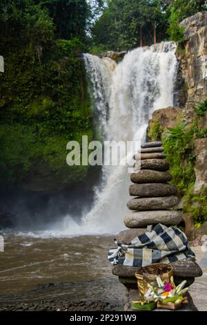 Gestapelte Steine mit balinesischen Angeboten vor dem Tegenungan-Wasserfall in Bali, Indonesien Stockfoto