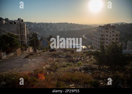 Ramallah steile Traumlandschaft mit einem schwarzen Auto geparkt, Bäume, Dschunken auf einem leeren Grundstück, eine leere Straße, die den Hügel hinuntergeht mit einem Linsenfeuer, Stockfoto