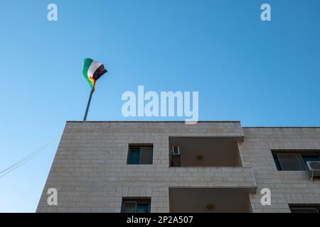 Ramallah, Ramallah und al-Bireh-Gouvernement, Palästina - 23. Juli 2022: Gebäude aus weißem Stein mit palästinensischer Flagge gegen klaren blauen Himmel in der Abenddämmerung Stockfoto