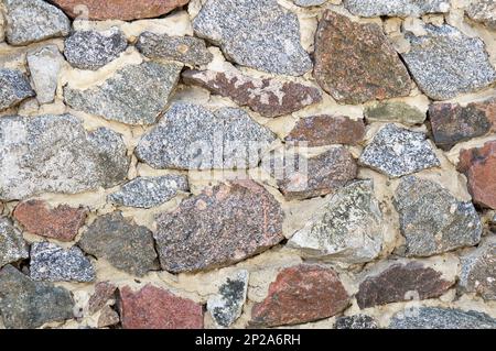 Die Struktur einer Steinwand aus grauem Granit verschiedener Größen und Formen. Altes Mauerwerk aus Schutt. Stockfoto
