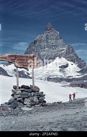 Bahnhof Trockener Steg mit Skifahrern im Sommer und Wegweiser zur Gandegghütte. Zermatt, Visp, Kanton Wallis, Schweiz, 1975 Stockfoto