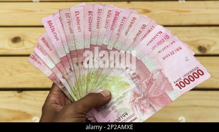 Die Hand eines Mannes enthält 100.000 Rupiah-Scheine. Indonesische Rupiah-Gelder, etwa 100.000 indonesische Gelder werden in menschlichen Händen gehalten. Stockfoto