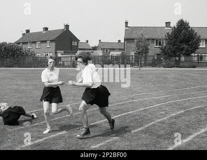 1989, am Sporttag der Sekundarschule, draußen auf einer Rasenbahn, Seniorinnen, die an einem Staffelrennen teilnehmen, ist einer gefallen, England, Großbritannien Stockfoto