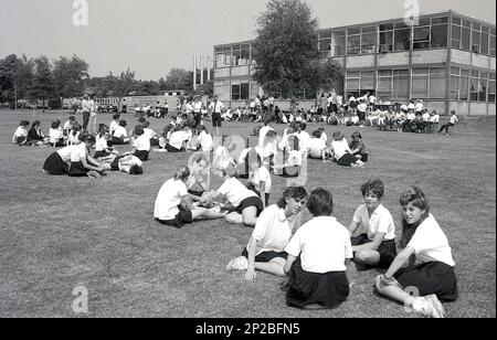 1989, Schulsporttag, tagsüber und Gruppen von Schülern der Sekundarstufe, die auf dem Rasen außerhalb des Schulgebäudes sitzen und eine Pause von der Athletik, England, Großbritannien, machen Stockfoto