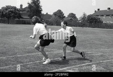 1989, am Sporttag der Sekundarschule, draußen auf einer Grasstrecke, nahmen zwei Mädchen im Teenageralter an einem Staffelrennen Teil, eine übergab den Stab an die andere, England, Großbritannien Stockfoto