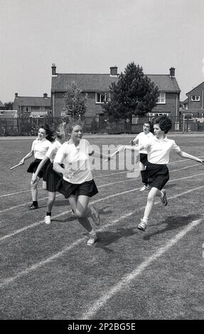 1989, Sporttag in der Sekundarschule, draußen auf einem Sportplatz, junge Teenager, die in einem Staffelrennen laufen und ihren Teamkollegen, England, Großbritannien, den Stab übergeben. Stockfoto