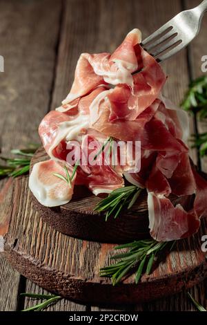 Italienischer Prosciutto oder spanischer Jamon mit Rosmarin auf einem alten Holztisch. Stockfoto