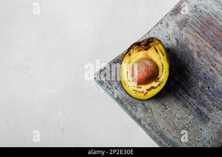 Verdorbene Avocado, überreife, schlechte Avocado auf dem Schneidebrett. Halb geschnittenes Obst, Freegan-Food-Konzept, grauer Hintergrund. Das Thema des vorsichtigen Konsums an Stockfoto