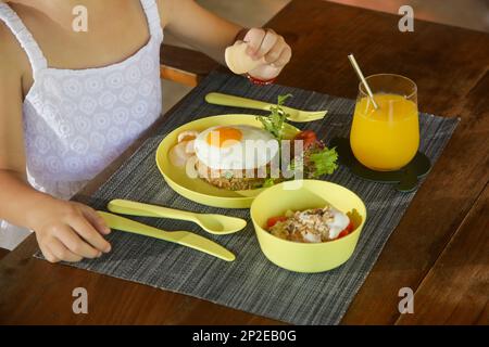 Kindermenü - sonnige Seite nach oben, Reis, grüner Salat und Müsli mit Joghurt serviert auf dem Restauranttisch mit kinderfreundlichem Plastikbesteck. Stockfoto