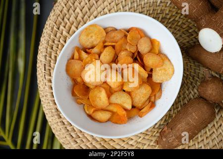 Indonesische Kassava-Chips in der Schüssel und Tapiokawurzel. Beliebte scharfe Yuca-Chips. Blick von oben. Stockfoto