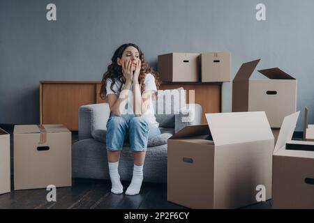 Müde junge Frau, die am Umzugstag in der Nähe von Pappkartons saß und eine Pause beim Packen hatte. Aufgebrachte geschiedene Frau beginnt ein neues Leben in Bewegung Stockfoto