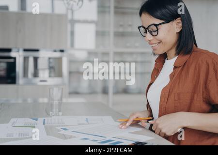 Lächelnde Geschäftsfrau mit Brille, die statistische Daten analysiert, die an Finanzprojekten oder Startup-Präsentationen arbeiten. Eine nette Angestellte, die das Dokum überprüft Stockfoto