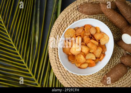 Indonesische Kassava-Chips in der Schüssel und Tapiokawurzel. Beliebte scharfe Yuca-Chips. Blick von oben. Stockfoto