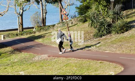 Vater brachte seiner Tochter Skateboarden auf einem Radweg bei, an einem sonnigen Tag Stockfoto